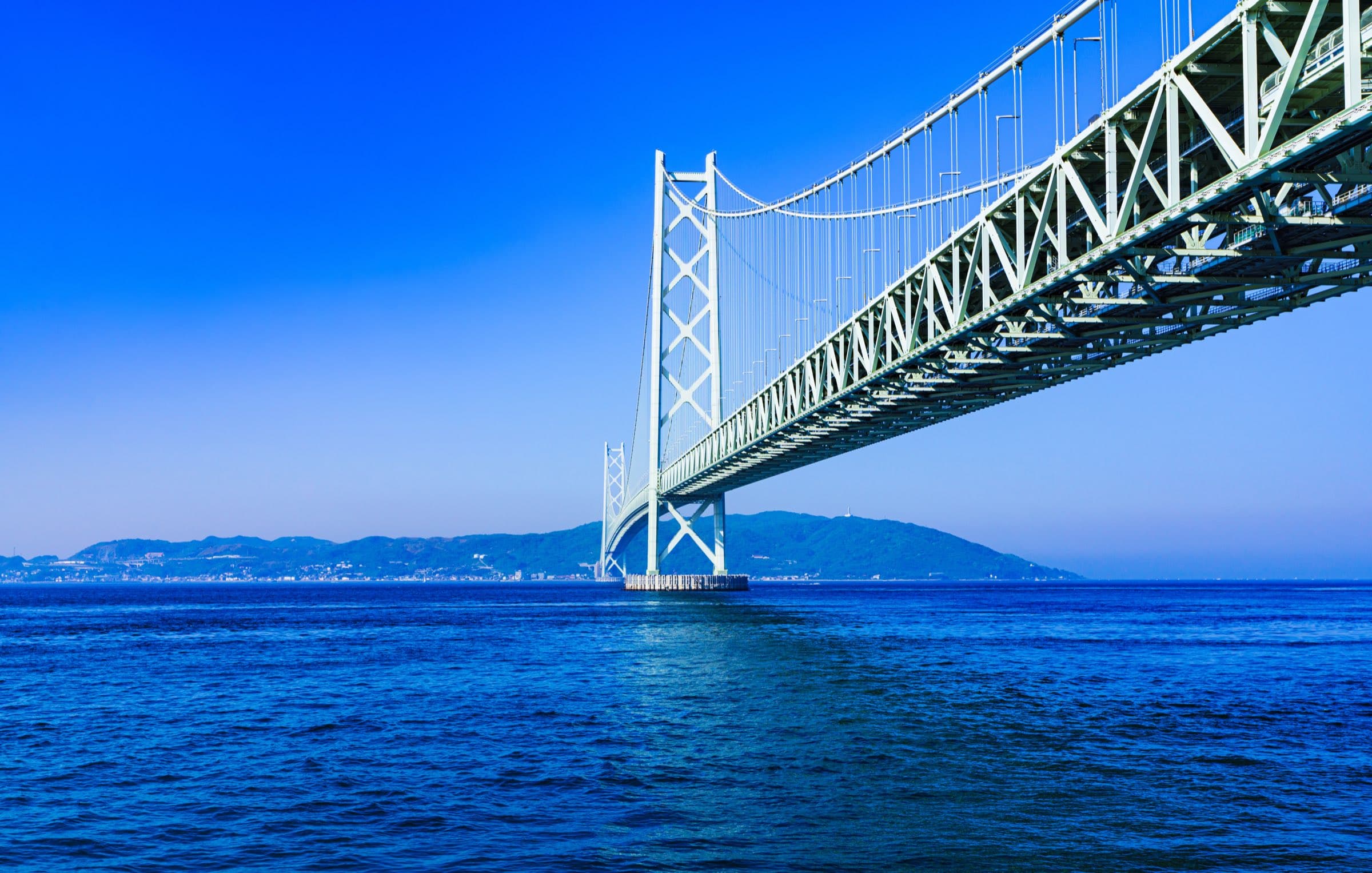 A suspension bridge spanning open water under a clear blue sky