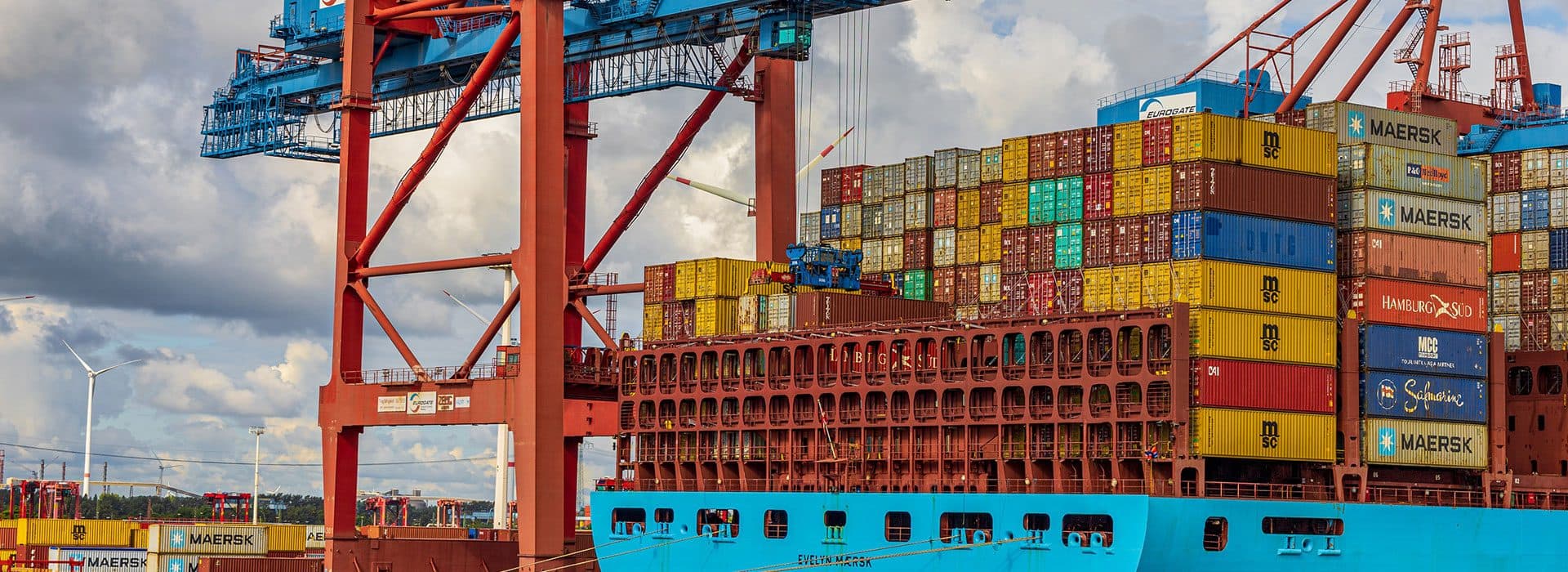 A container ship being loaded by cranes at a port terminal, stacked with shipping containers